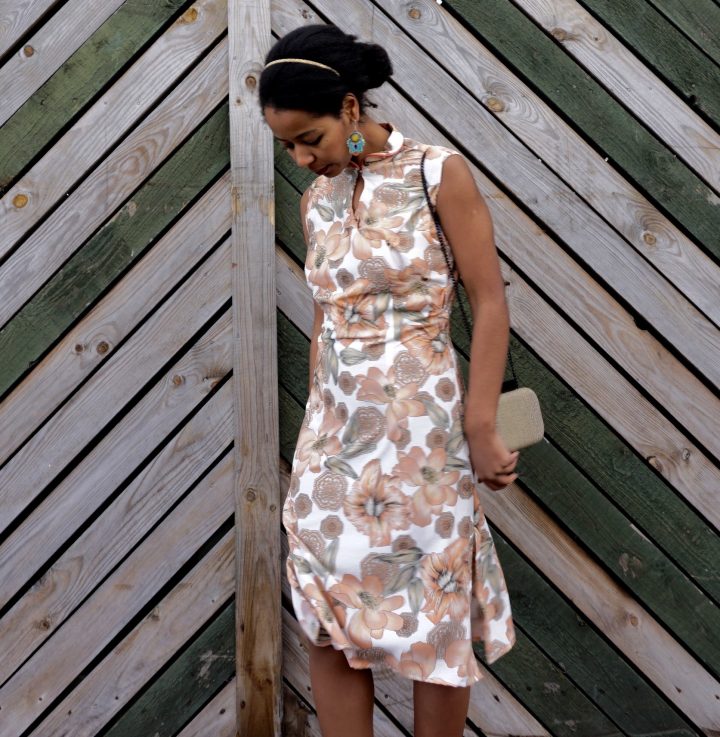 Megan is standing against a fence. She is wearing her handmade qipao. The fabric has a floral print..